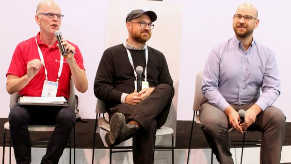 Three people sitting on a stage have a discussion at a conference